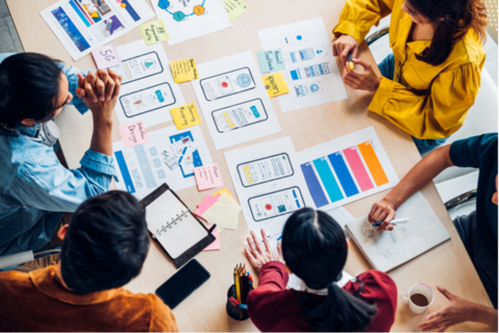 A user experience team using a whiteboard with post it notes to design a mobile app